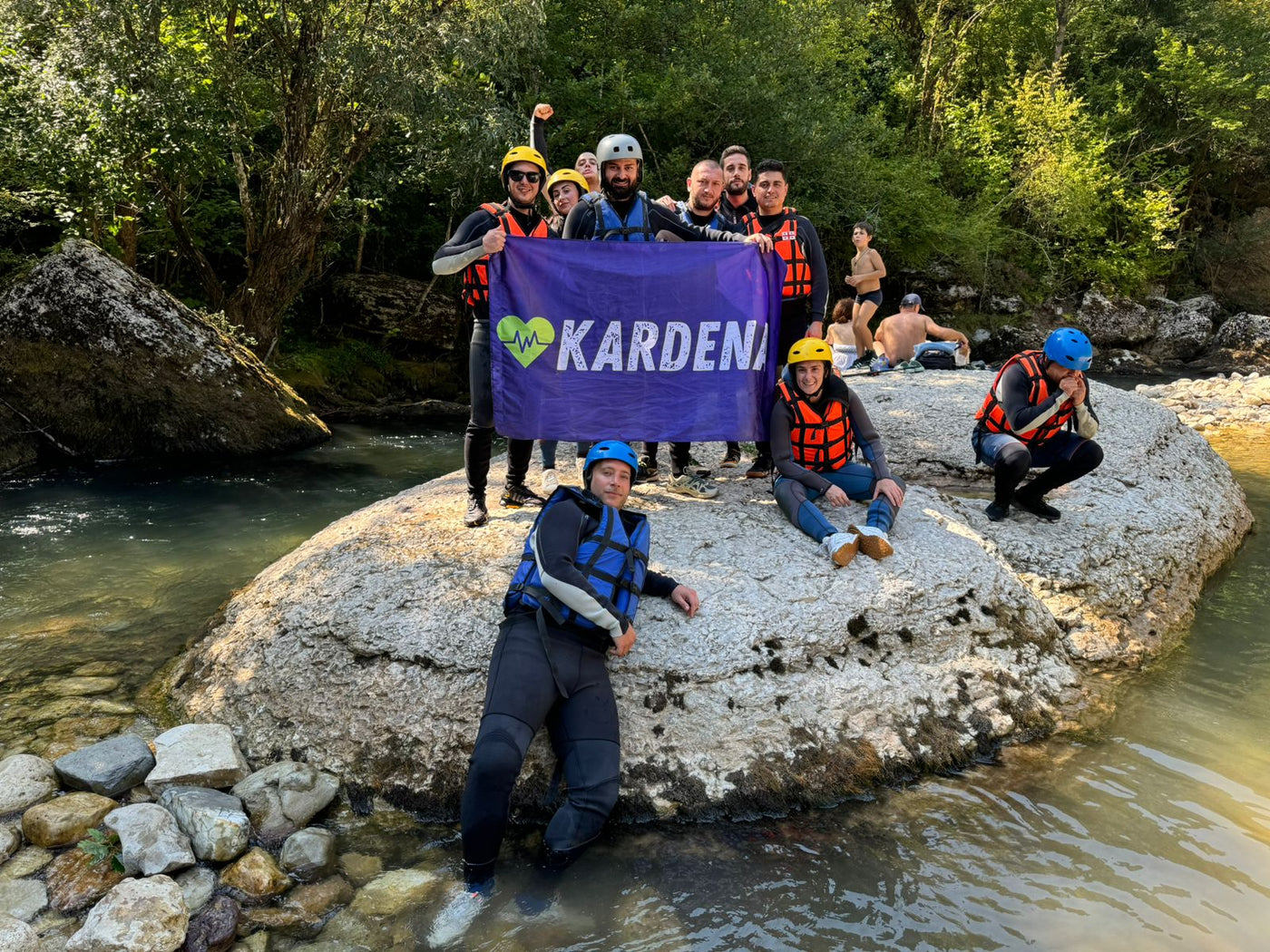 Gruppe mit Kardena-Flagge im Fluss, mit Helmen und Schwimmwesten für Outdoor-Abenteuer